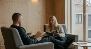 Casal sentado em poltronas confortáveis, lendo livros em um ambiente iluminado e aconchegante.