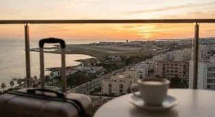 Maleta ao lado de uma xícara de café, vista do aeroporto e do pôr do sol em Florianópolis.