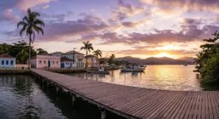 Pôr do sol sobre o Ribeirão da Ilha, com casas coloridas e barcos ancorados ao longo do cais de madeira.