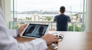 Homem olhando a paisagem da cidade enquanto médico analisa radiografia em tablet.