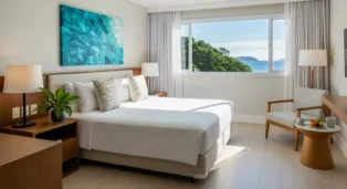 Quarto de hotel com cama de casal, janelas amplas e vista para o mar, decorado em tons claros.