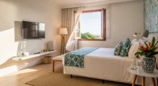 Quarto de hotel com cama confortável, decoração em tons claros e vista para a natureza através da janela.