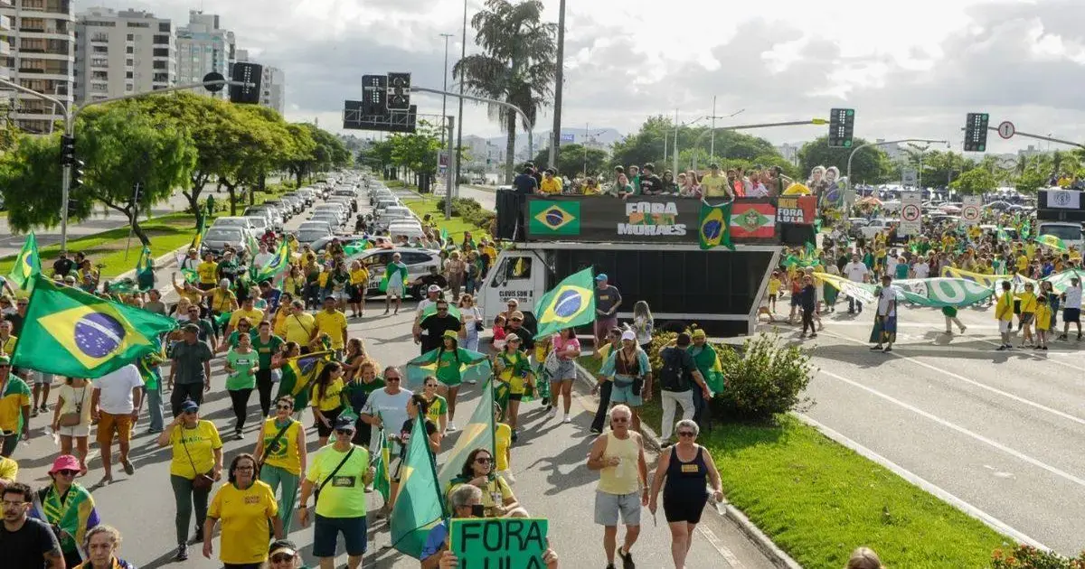 Ato ‘Acorda, Brasil’ reúne apoiadores e lideranças em Florianópolis Multidão de pessoas marcha em rua, segurando bandeiras do Brasil e cartazes com mensagens políticas.