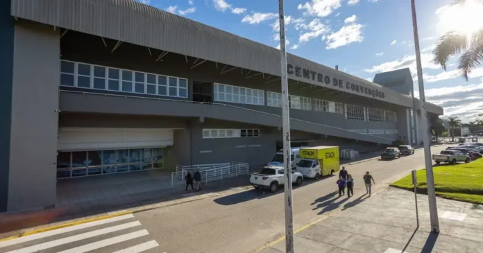 Centro de Convenções com pessoas caminhando pela calçada e veículos estacionados.