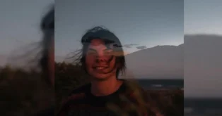 Pessoas sorrindo ao pôr do sol, com um cenário de montanha e mar ao fundo.