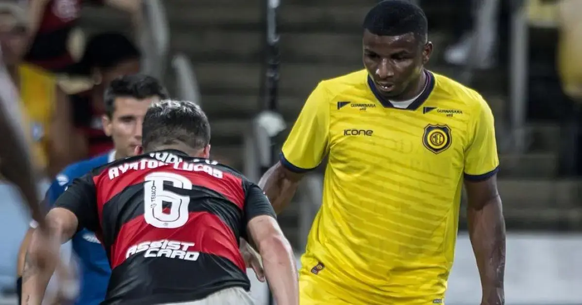 Atletas em campo, um em uniforme preto com o número 6 e outro em uniforme amarelo, em ação durante a partida.