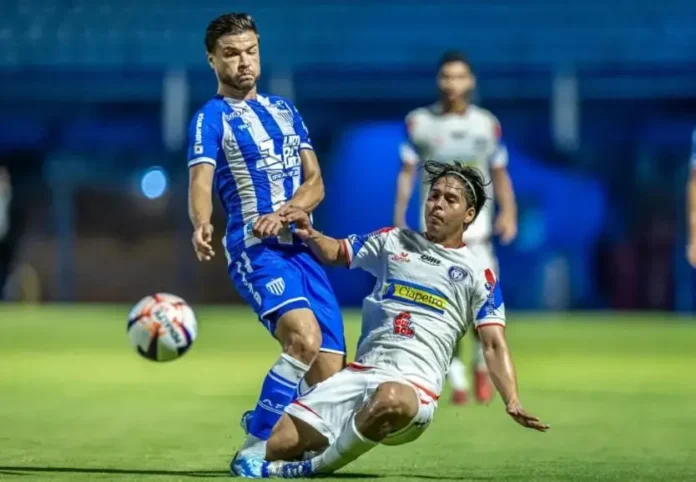 Dois jogadores de futebol em ação, um recebendo falta no campo, com a bola visível ao lado.