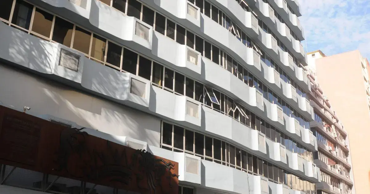 Fachada de um prédio com janelas em diferentes níveis e uma placa ao nível do solo.