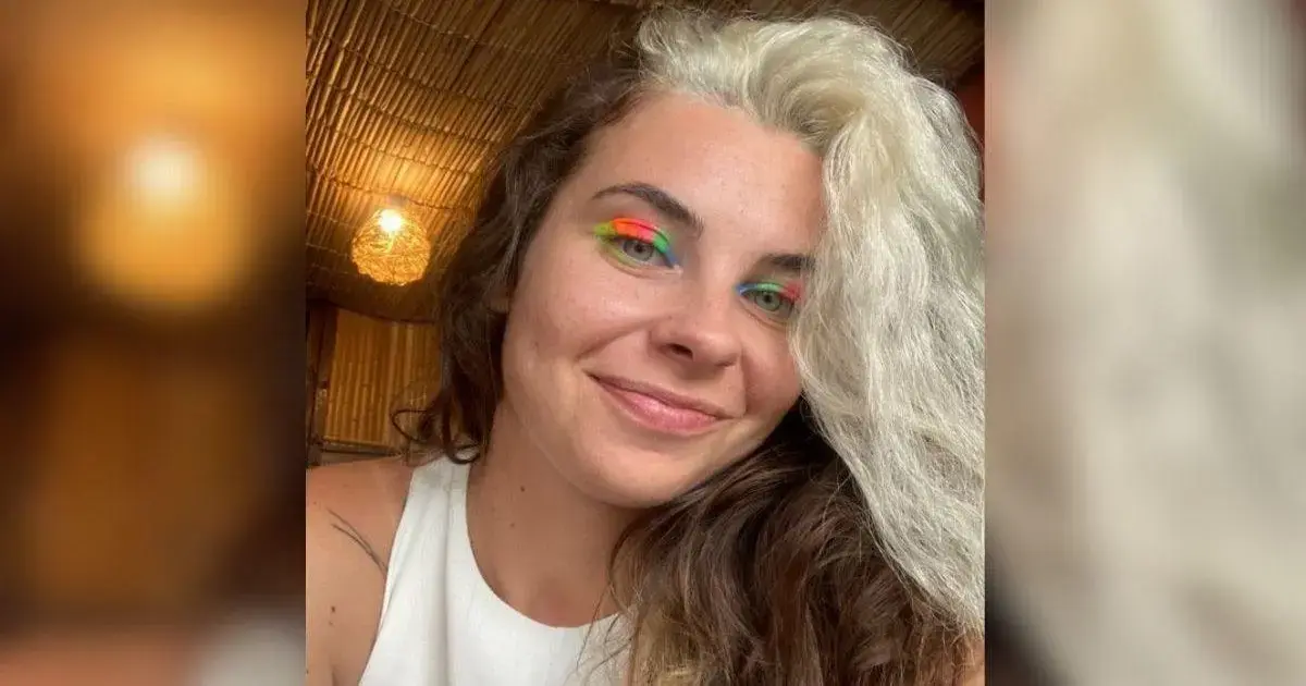 Mulher com cabelo claro e ondas, usando maquiagem colorida nos olhos em ambiente interno com luz suave.