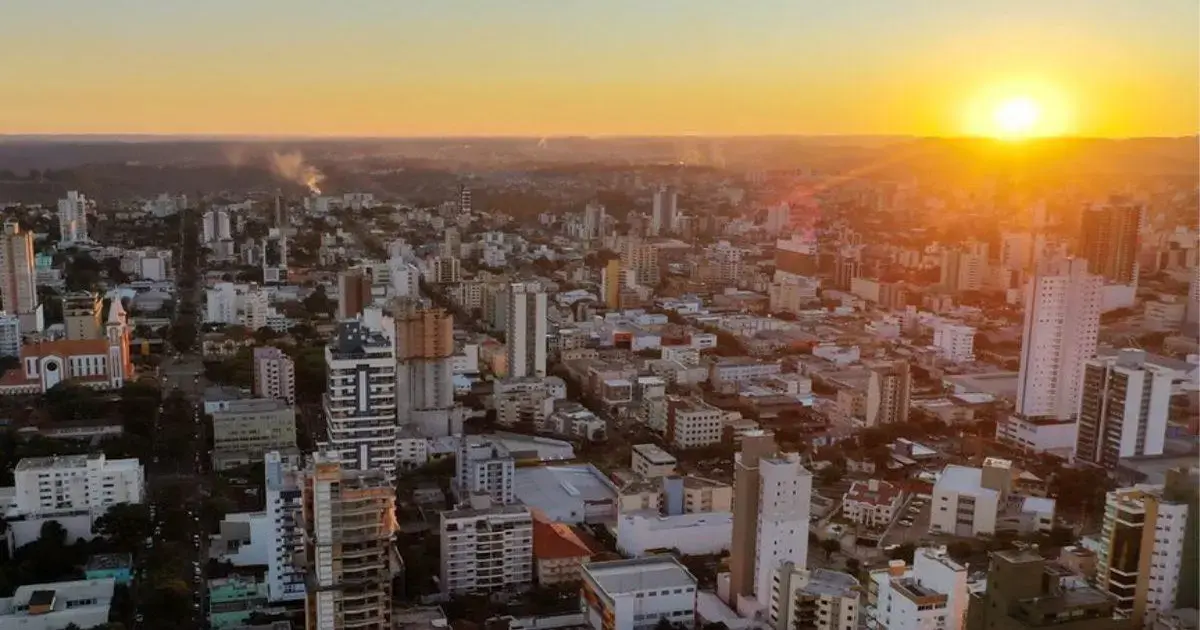 Vista panorâmica de uma cidade ao pôr do sol, com prédios e ruas visíveis.