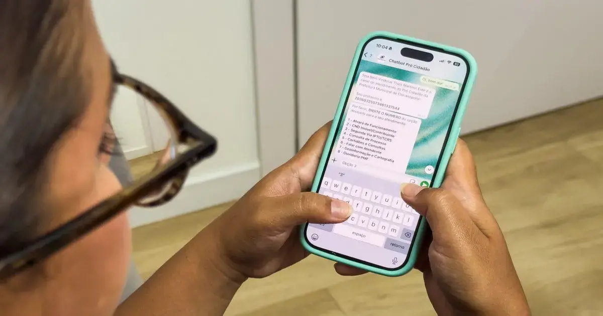 Pessoa segurando um celular com tela mostrando uma conversa no WhatsApp sobre o chatbot Pró-Cidadão.