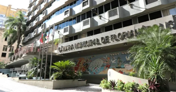 Fachada da Câmara Municipal de Florianópolis com plantas e bandeiras visíveis. Mural decorativo em destaque.