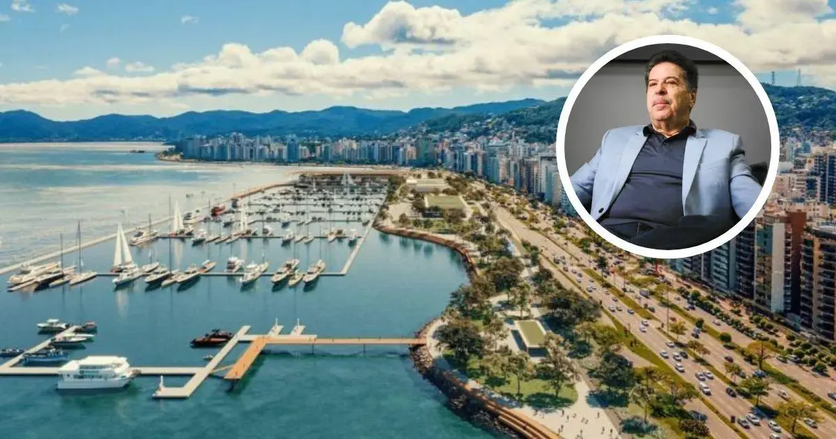 Vista aérea de uma marina com embarcações ancoradas e uma avenida com prédios à beira-mar.