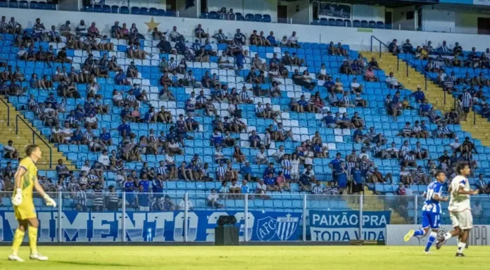 Torcedores em arquibancada de estádio com bandeiras, em campo jogadores de futebol em ação. Texto legível: "PAIXÃO PARA TODA VIDA".