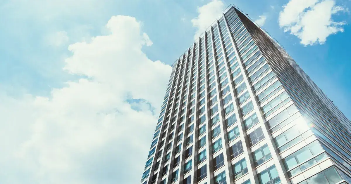 Edifício de estrutura moderna é visto de baixo, com céu azul e nuvens ao fundo.