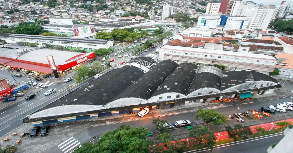 Vista aérea de um prédio com telhado arredondado, cercado por ruas, veículos e árvores em uma área urbana.