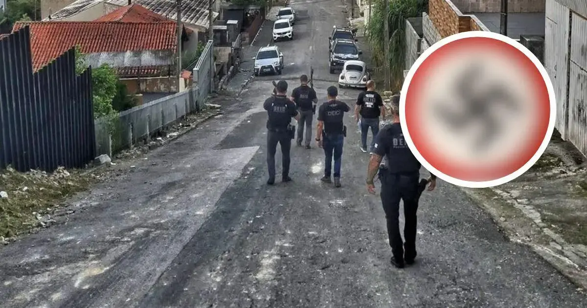 Agentes da polícia caminham em uma rua, enquanto veículos estão estacionados ao longe.