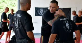 Grupo de policiais em treinamento, alguns com camisetas com a palavra "ALUNO", praticando técnicas de combate.