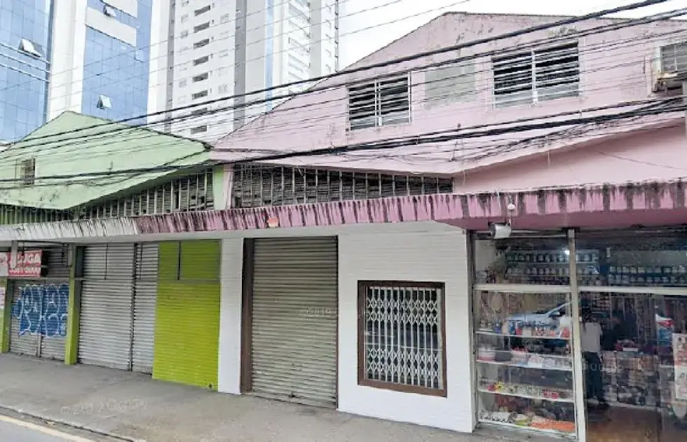 Edifícios comerciais com fachadas em tons de verde e rosa, arcos metálicos e janelas, em ambiente urbano.