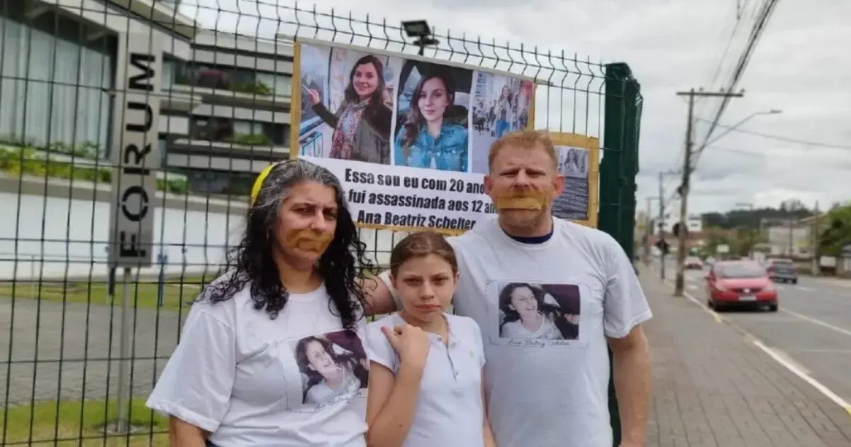 Mulher, menina e homem em frente a um fórum, com camisetas estampadas e cartaz sobre Ana Beatriz Schelter.