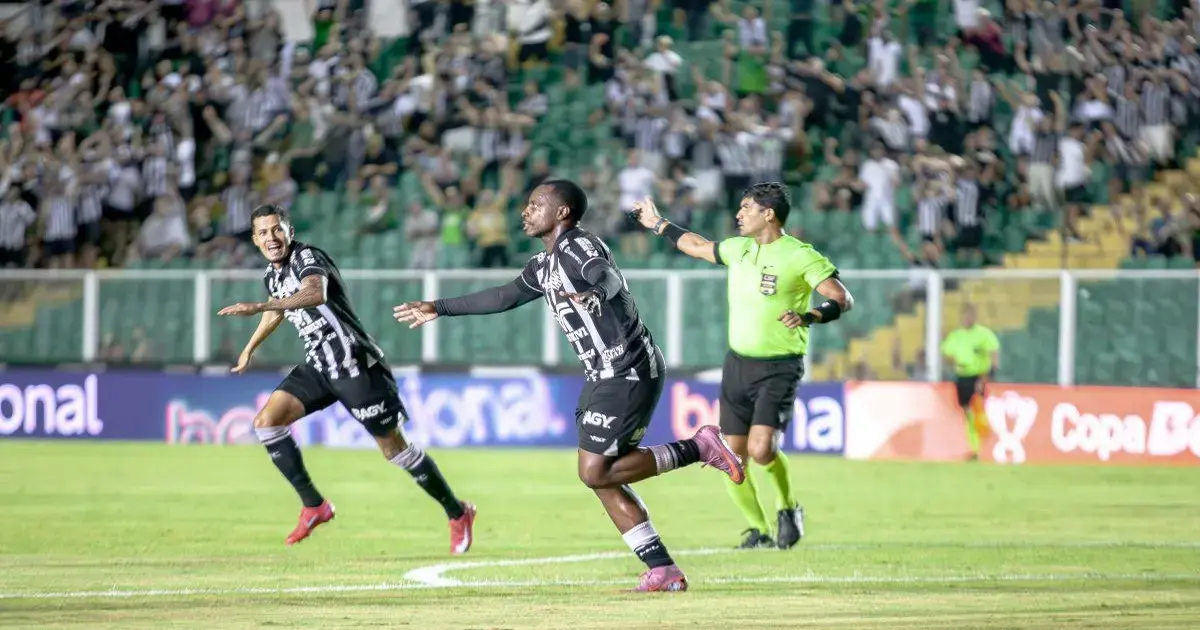 Figueirense avança na Copa do Brasil com premiações significativas Dois jogadores celebrando um gol em um jogo de futebol, enquanto um árbitro observa. A torcida ao fundo está animada.