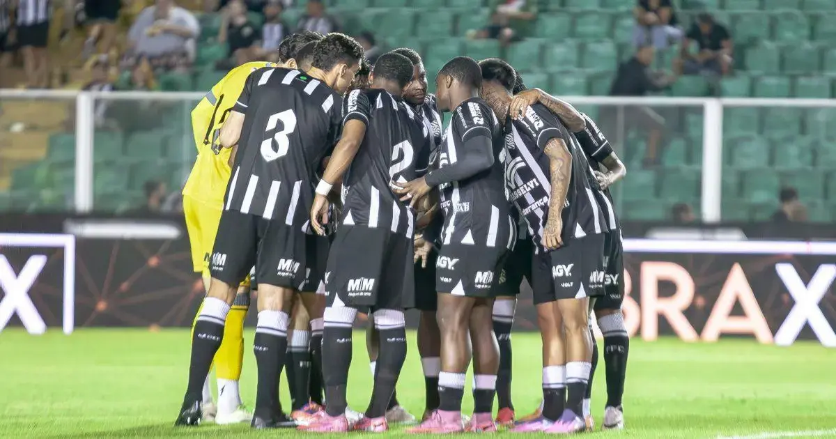 Jogadores de futebol em um círculo, se preparando para o jogo, em um campo iluminado.