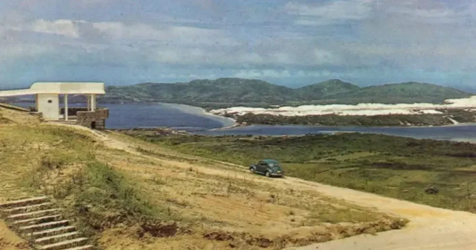 Construção em um terreno elevado com vista para o mar e montanhas, com um carro estacionado próximo.