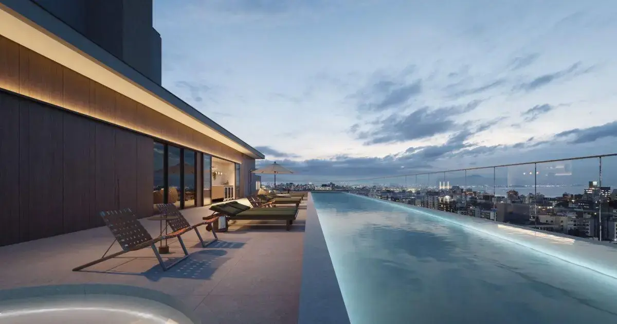 Florianópolis: ARKKI e o Futuro Habitacional Pôr do sol visto de uma piscina infinita em um terraço com espreguiçadeiras e uma cidade ao fundo.