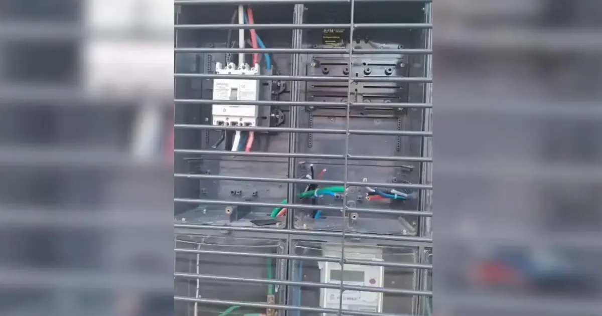 Painel elétrico com fiações expostas, dispositivos de proteção e medidor de energia visível na parte inferior.