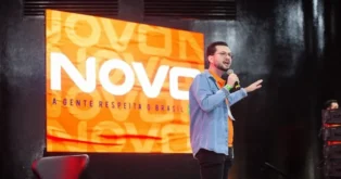 Público em um evento, com uma pessoa falando ao microfone e um painel atrás, exibindo a palavra "NOVO" e a frase "A GENTE RESPEITA O BRASIL".