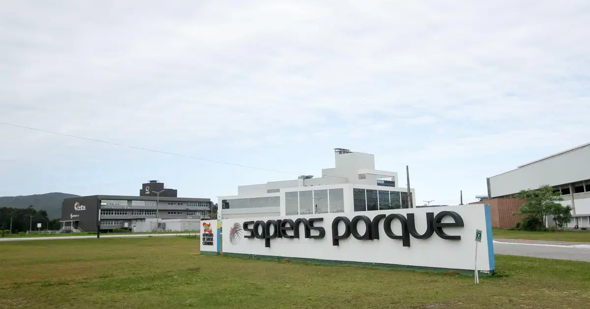 Sinal de entrada do Sapiens Parque em Florianópolis, com edifícios de vidro e gramado ao redor.