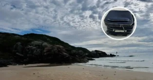 Praia com céu nublado, rochas à beira-mar e uma mala de viagem em destaque.