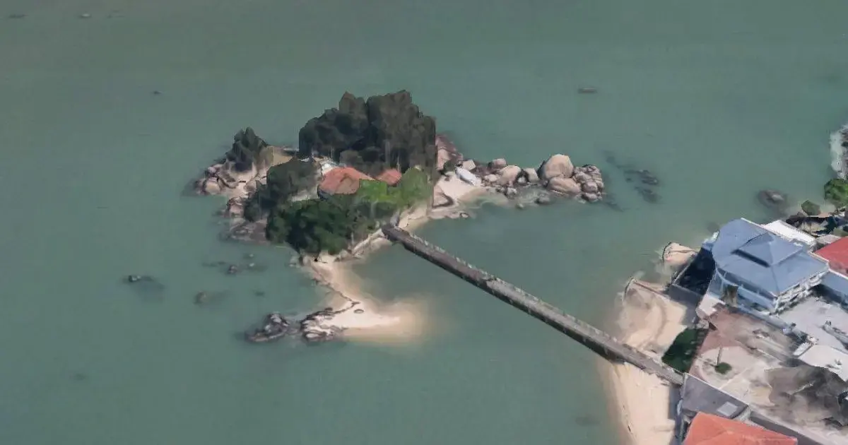 Ilha da Saudade é arrematada em leilão em Florianópolis Ilha com vegetação e construção acessada por passarela, cercada por água e pedras.