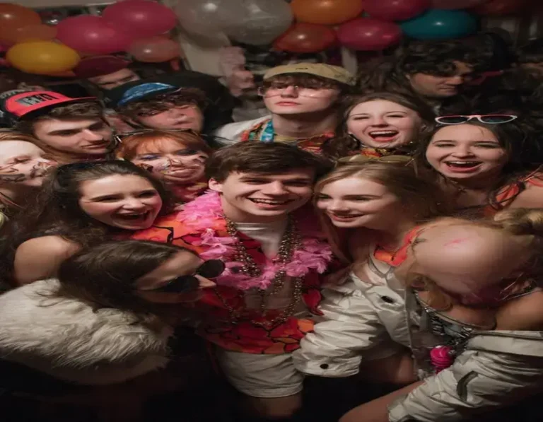 Grupo de pessoas sorrindo em uma festa, com balões coloridos e decoração festiva ao fundo.
