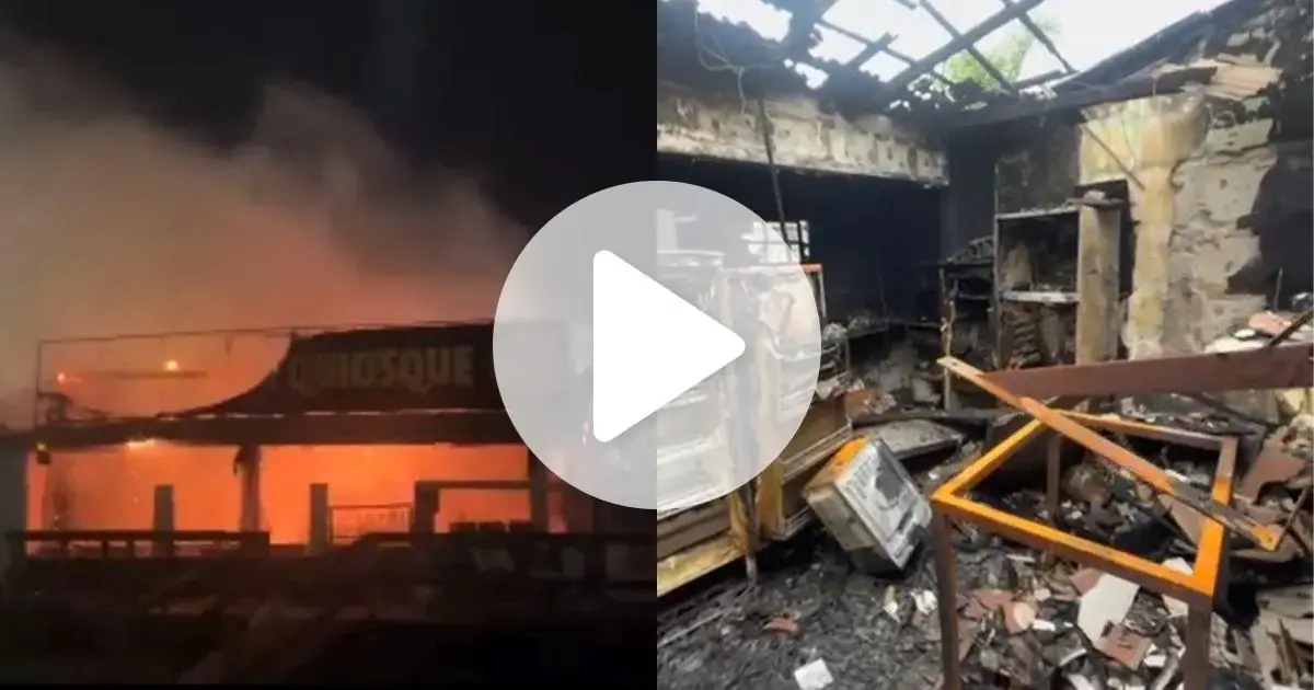 Fogo consumindo quiosque, com estrutura parcialmente destruída e restos de móveis queimados visíveis no interior.