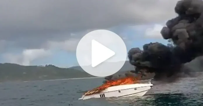 Lancha em chamas no mar, soltando fumaça preta, enquanto as ondas estão ao redor.