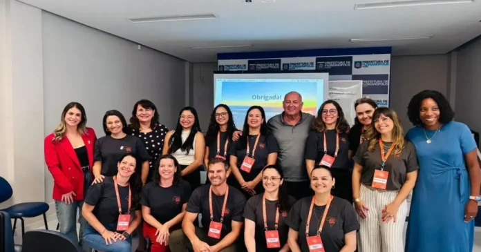 Grupo de pessoas sorrindo em ambiente interno, com painel ao fundo exibindo a palavra "Obrigada!".