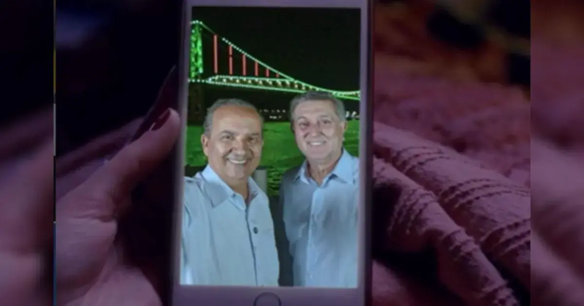 Jorginho Mello e Topázio Neto: tensões políticas em Santa Catarina Duas pessoas sorrindo em uma selfie com uma ponte iluminada ao fundo.