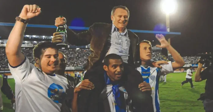 Grupo de quatro pessoas celebrando no campo, uma delas é levantada por outras, segurando uma garrafa.