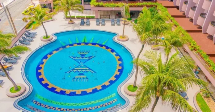Área da piscina com padrão decorativo em azul e amarelo, rodeada por espreguiçadeiras e palmeiras.