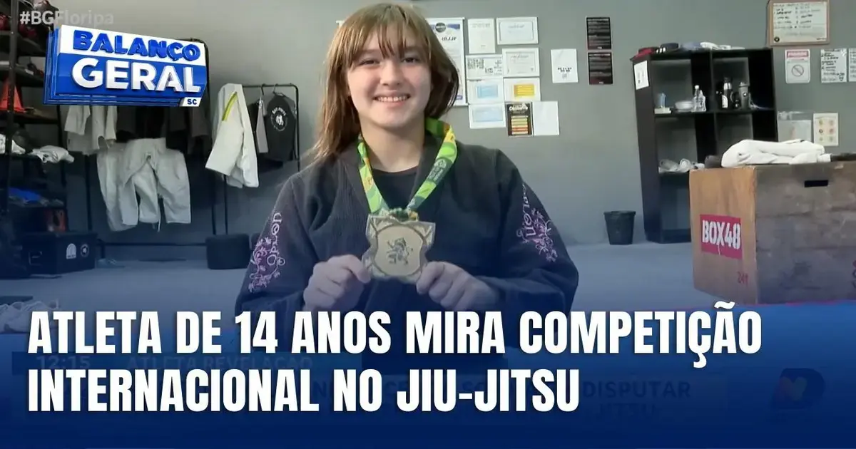 Atleta de jiu-jitsu segura medalha em ambiente de treinamento, com prêmios e quimonos ao fundo.