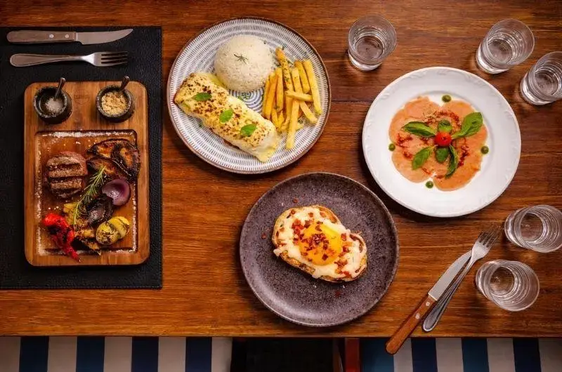 Los Troncos Parrilla Uruguaya lança menu saudável em Florianópolis Prato com carnes, legumes grelhados, arroz e fritas, além de pratos adicionais em uma mesa de madeira.