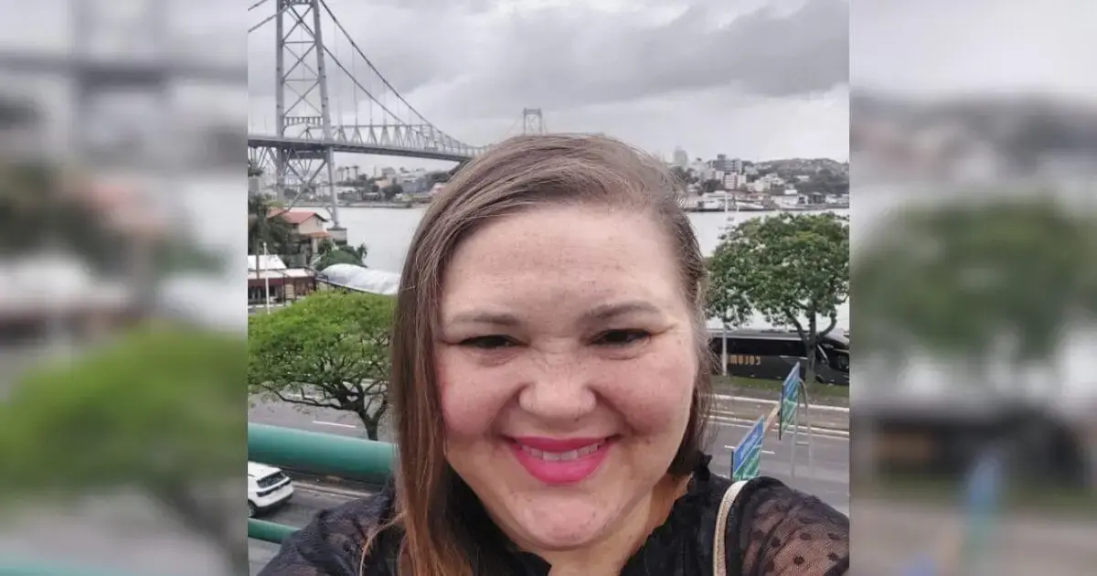Retrato de uma pessoa sorrindo em frente a uma ponte e um rio, com nuvens no céu.