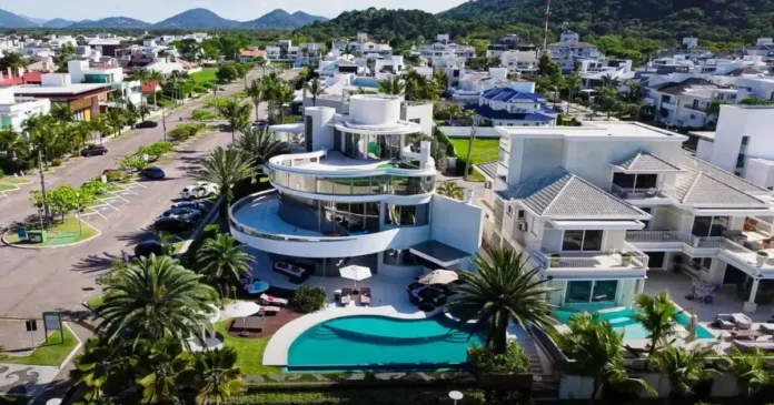 Vista aérea de uma mansão moderna com piscina, cercada por palmeiras, em uma área residencial.