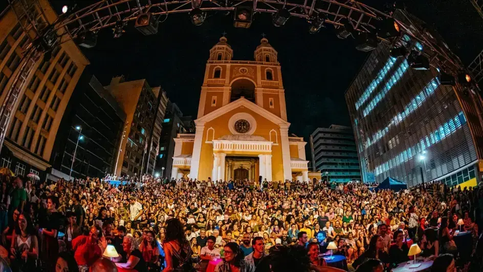 Maratona Cultural de Florianópolis traz teatro e dança em programação intensa Público reunido em praça durante apresentação noturna em frente a uma igreja, cercada por prédios.