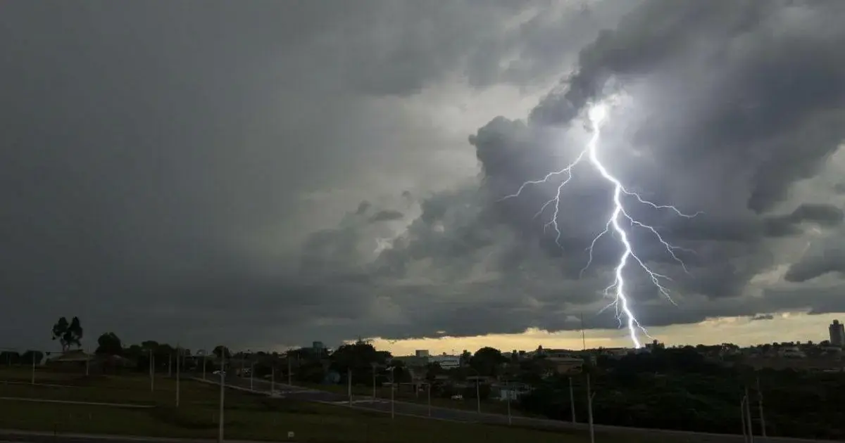 Relâmpago ilumina o céu encoberto por nuvens escuras, com uma cidade visível no fundo.