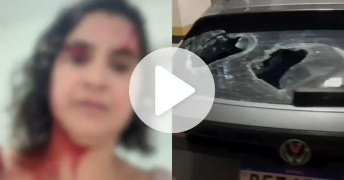 Mulher com ferimentos na cabeça, sangue visível, e veículo com vidro quebrado.