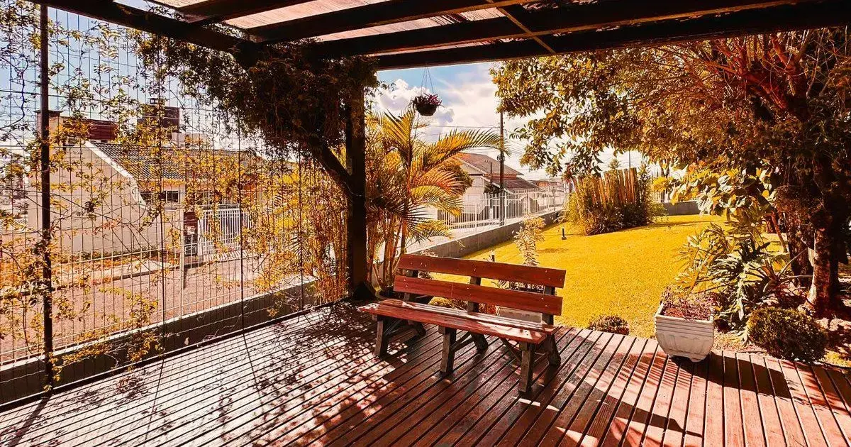 Espaço ao ar livre com um banco de madeira, plantas ao redor e gramado verde sob luz solar.