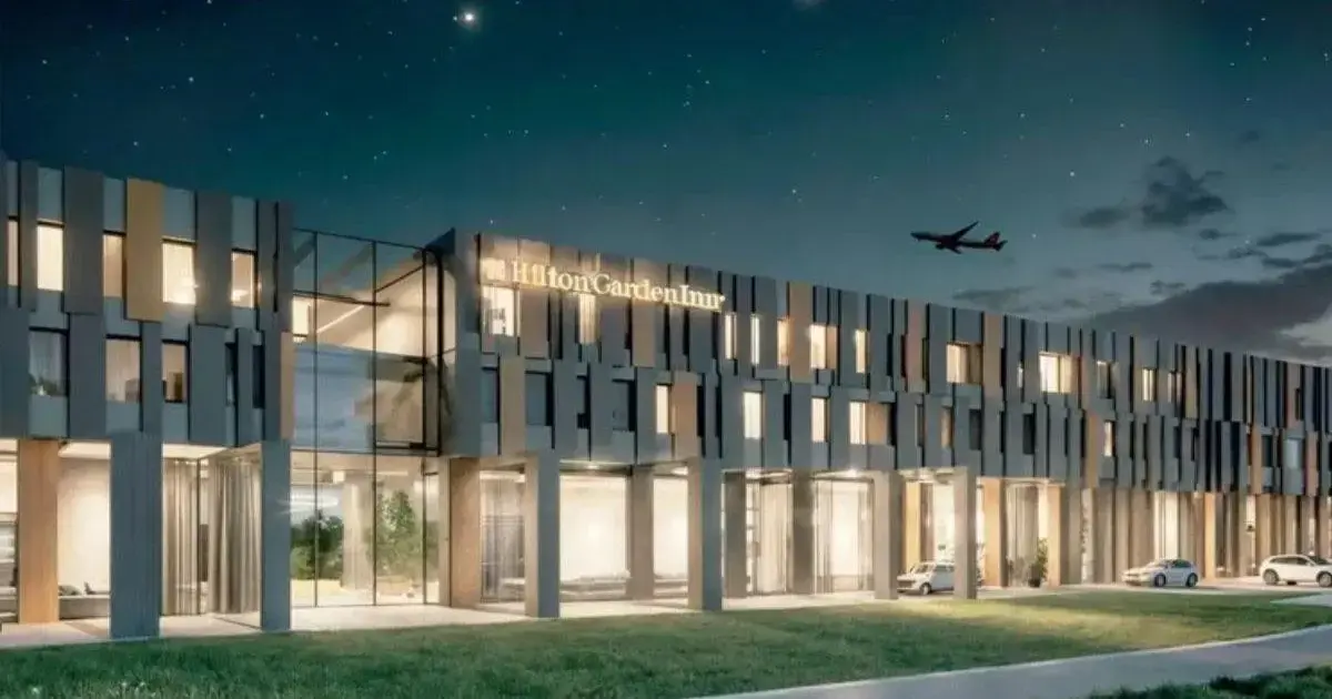 Novo Hotel Hilton em Florianópolis até 2028 Fachada do hotel Hilton Garden Inn iluminada à noite, com carinhas em um fundo estrelado e um avião no céu.