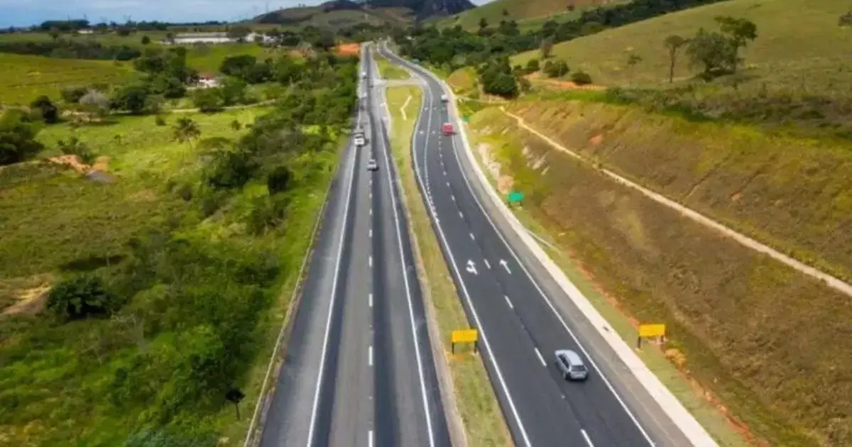 Obra da Rodovia Via Mar será Iniciada em 2026 Trecho de rodovia com veículos em movimento, cercado por áreas verdes e colinas ao fundo.